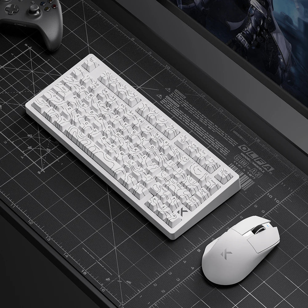 White mechanical keyboard and matching mouse on grid desk mat, gaming setup with controller and monitor